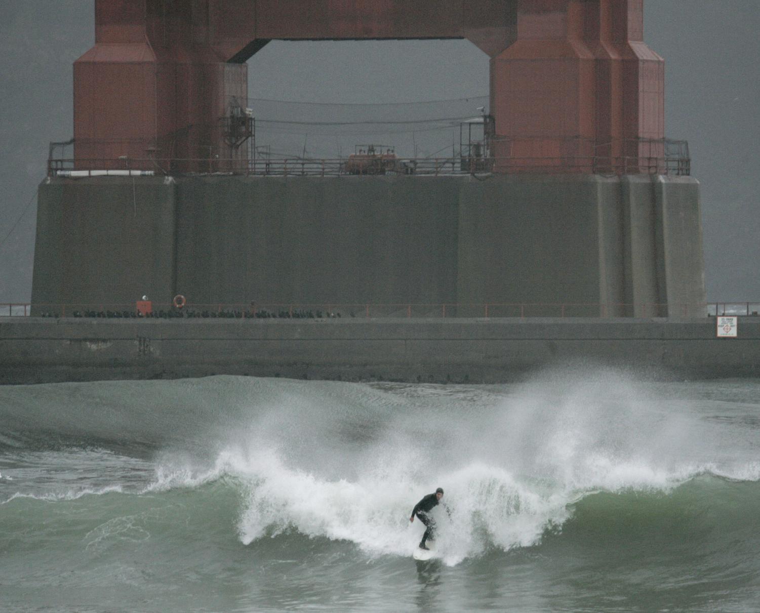 A surfer rides a wave churned by a winter storm underneath the south tower of the Golden Gate Bridge Friday, Jan. 4, 2008, in San Francisco Bay.