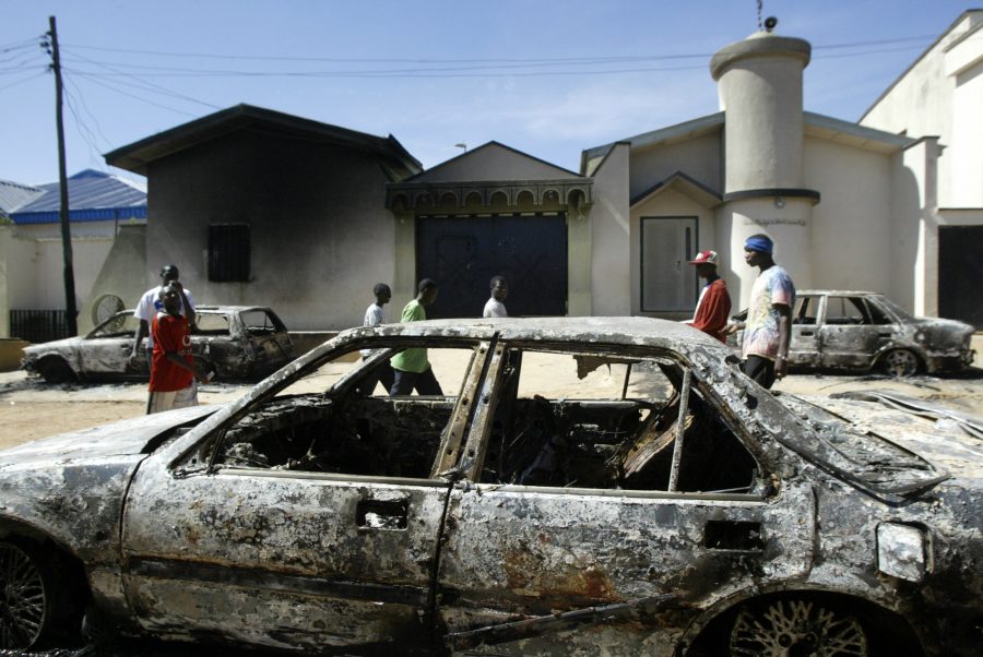  People walk past destroyed cars following two days of deathly rioting in Jos, Nigeria, Monday, Dec. 1. Daily life began returning to normal Monday in the city after two days of election-related violence, which is reported to have killed more than 300 people. Photo by Courtesy: AP