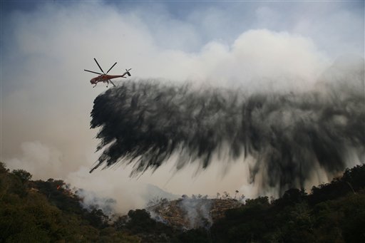 A helicopter makes a water drop as firefighters battle the Station wildfire burning in the Angeles National Forest northeast of downtown Los Angeles on Firday, Aug. 28. The Los Angles Sheriffs Department says a voluntary evacuation is being urged for nearly 900 homes in the La Canada Flintridge area. (AP Photo/Jason Redmond)