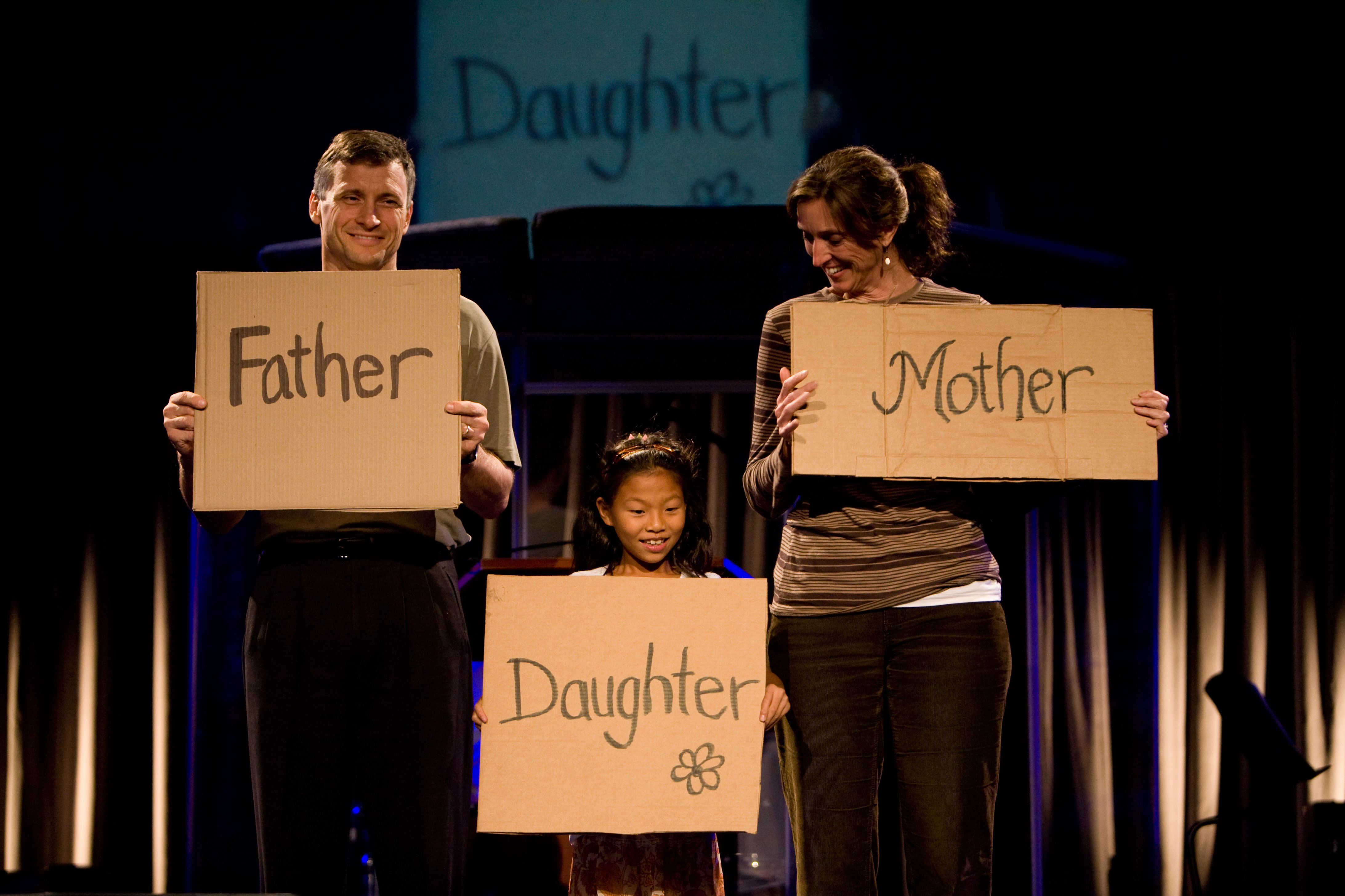 Erik and Donna Thoennes, both Biola professors, hold up signs with their daughter, Caroline Thoennes, during a procession of cardboard sign testimonies at Wednesday's final Torrey Conference session. The couple, after being childless for 19 years, adopted Caroline from Taiwan two summers ago.