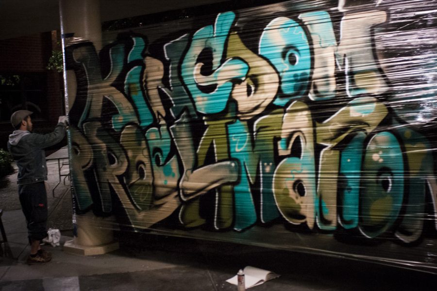 A graffiti artist puts the finishing touches on his piece, Kingdom Proclamation, outside Sutherland Auditorium on Friday night. | Grant Walter/THE CHIMES