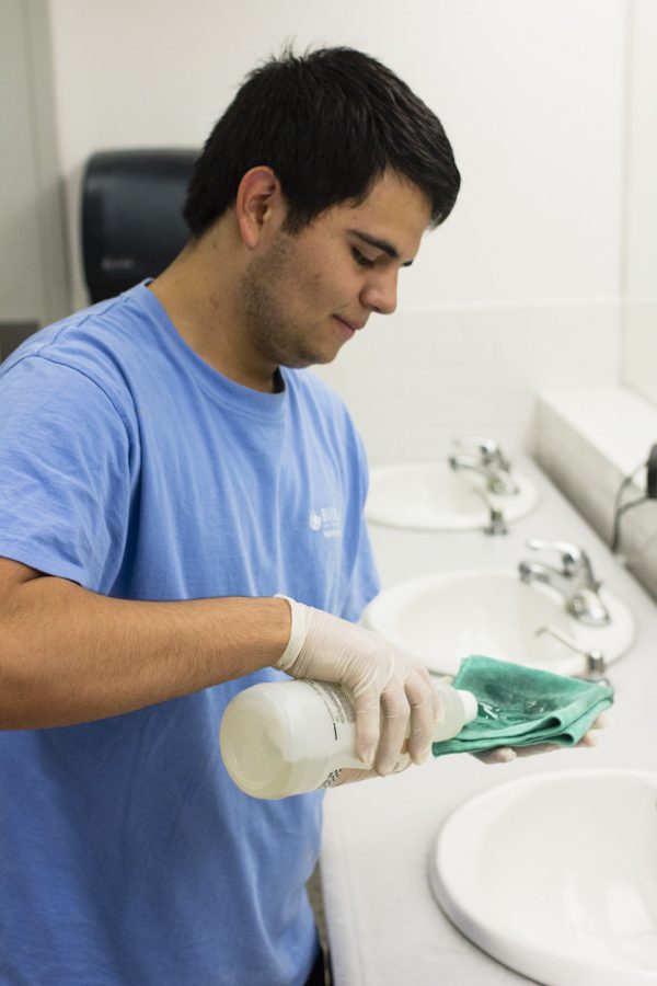 Sophomore Steven Orozco wipes down a bathroom door during his shift as a facilities worker on campus. He, like other full-time student employees, are at risk of getting hours cut.  | John Buchanan/THE CHIMES