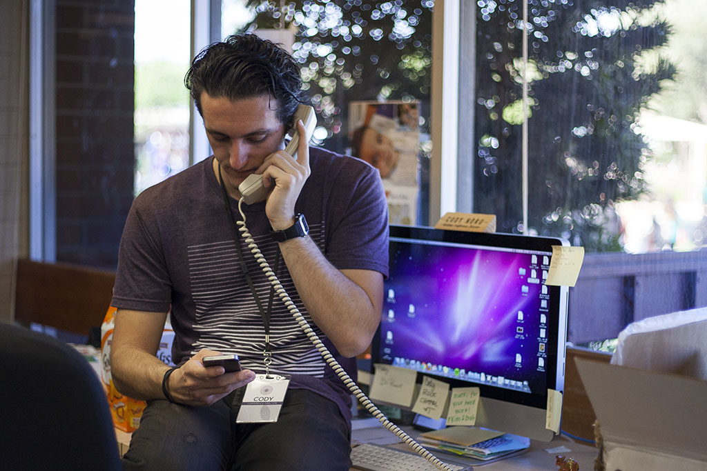 Nord answers the SMU office phone while texting a coordinator. A majority of Nord's day involved troubleshooting. | Melanie Kim/THE CHIMES