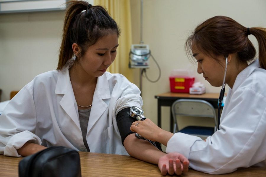 Nursing students Jin Lee and Eunice Lee practice taking each others blood pressure. Students involved in the nursing program are now preparing to serve overseas. | Aaron Fooks/THE CHIMES