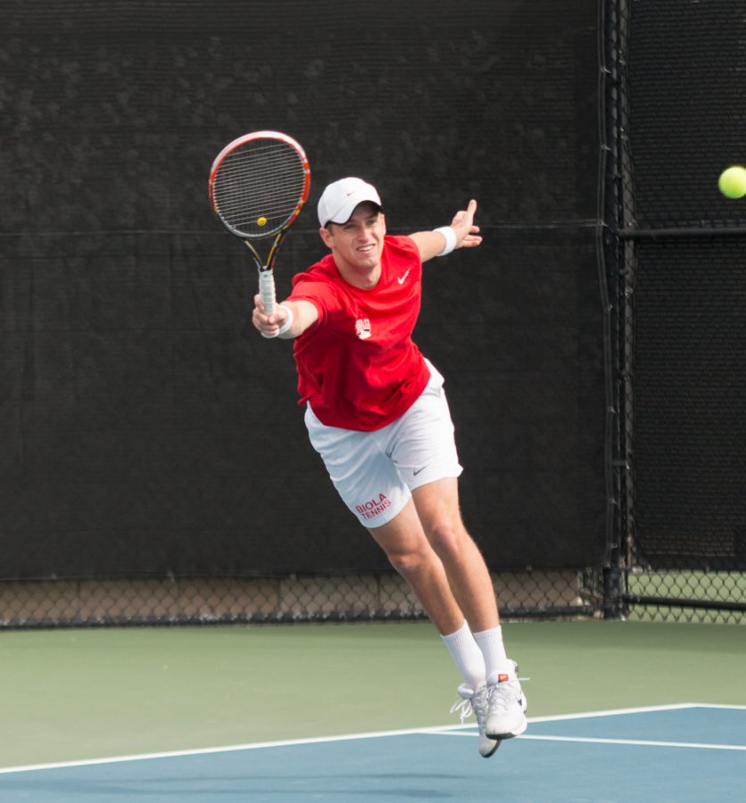 Sophomore Luke Mountain jumps up for the ball to strike during the tennis match this weekend. | Aaron Fooks/THE CHIMES