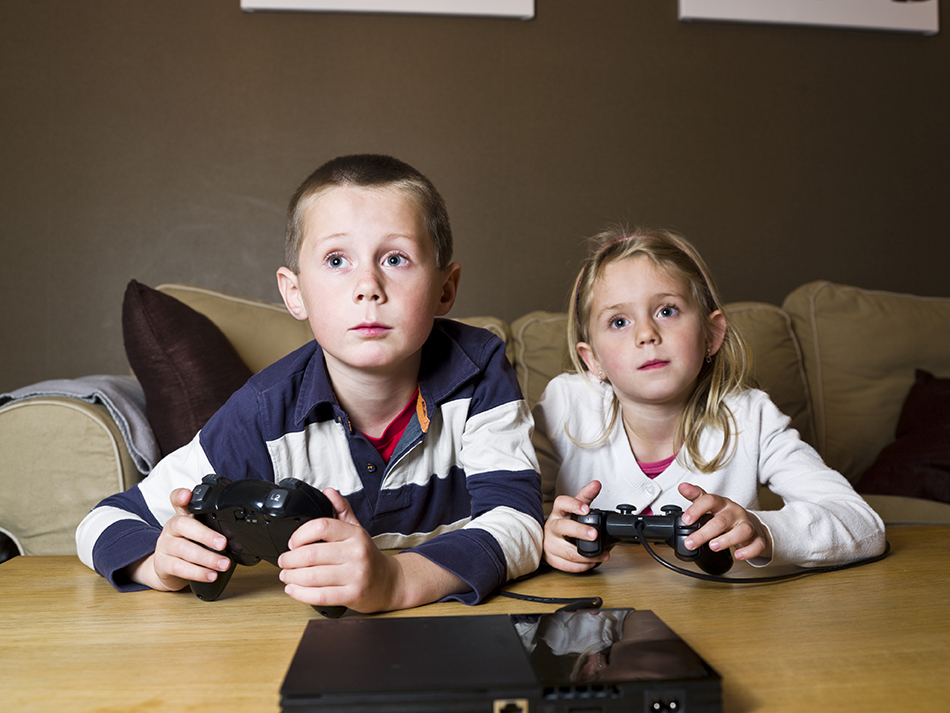 Siblings playing Video Games sitting in the sofa