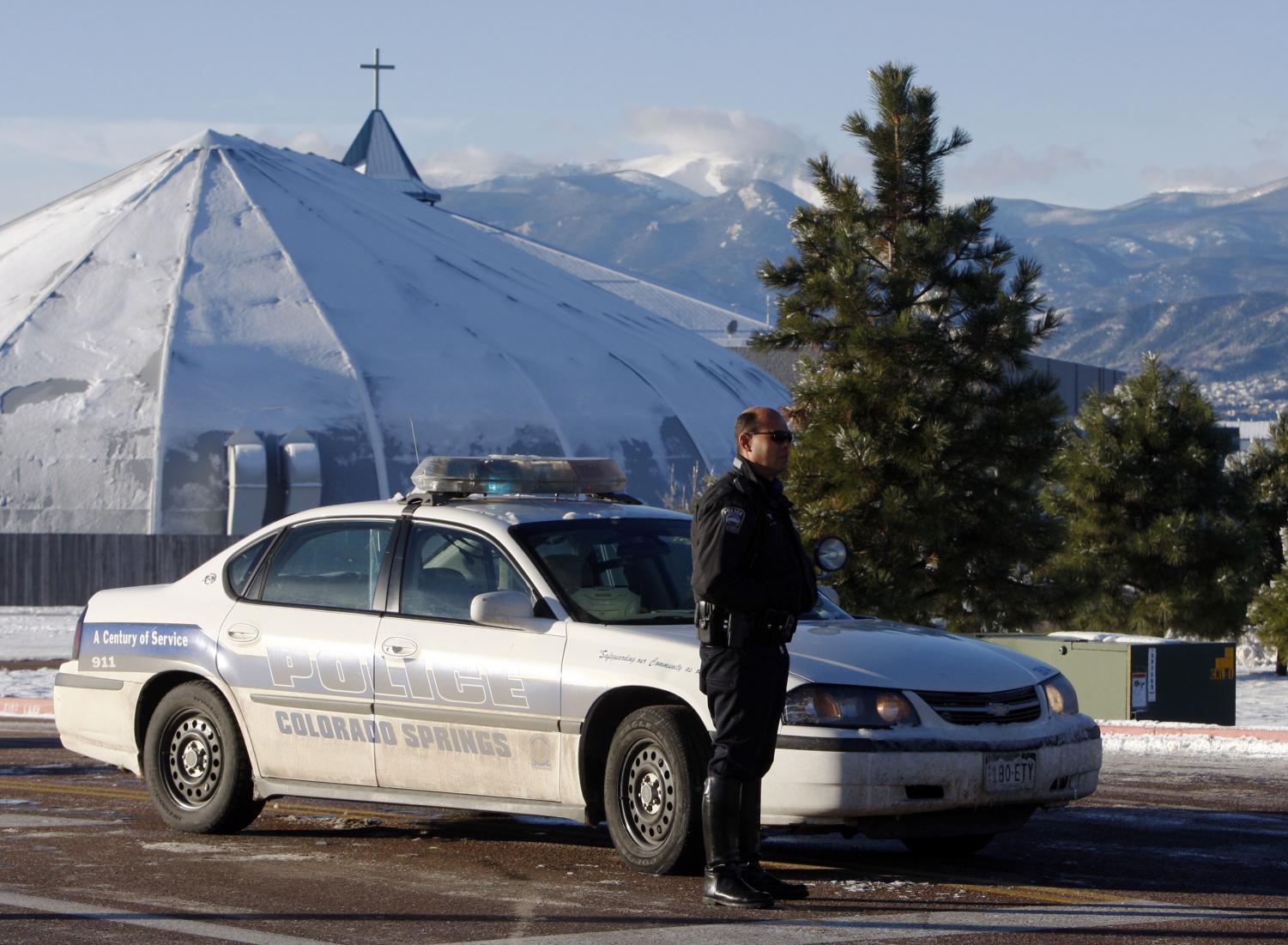 An unidentified officer stands by his cruiser while blocking the roadway into the New Life Church on Dec. 10. Two women died from a shooting at the church, which was one of two church shootings in Colorado on Sunday.