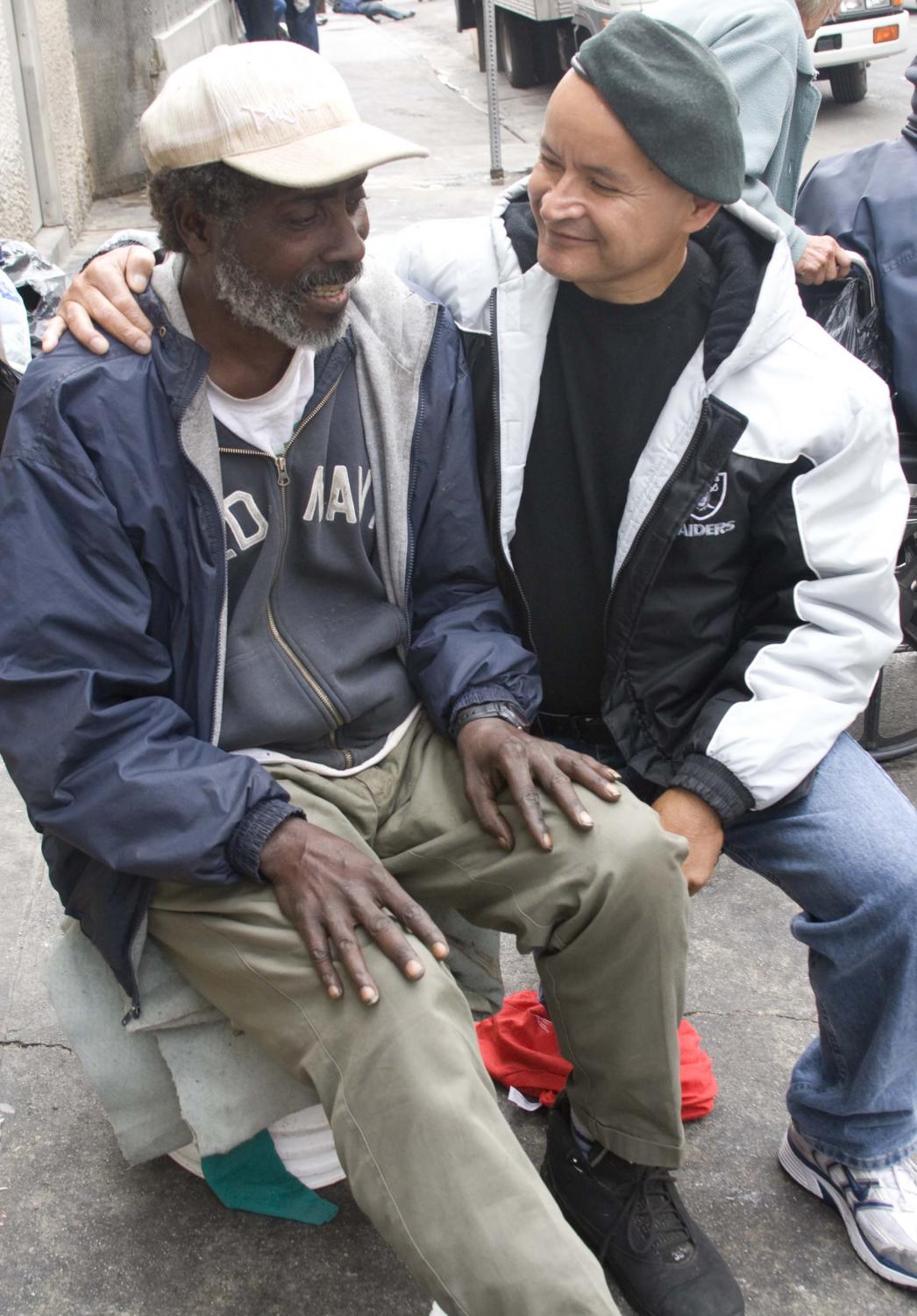 Henry A.K.A Thunder, turned 57 years of age today, sits on bucket on the sidewalks of Skid Row while ex-skid row resident and new Biola student, Jose Villalpando ministers to him.