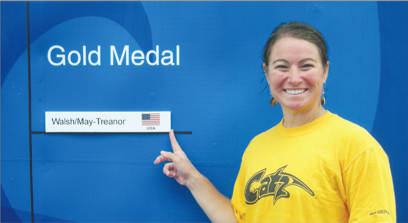 Anya Tronson poses for a picture next to the final gold medal bracket, showing the winners of the women's beach volleyball event.