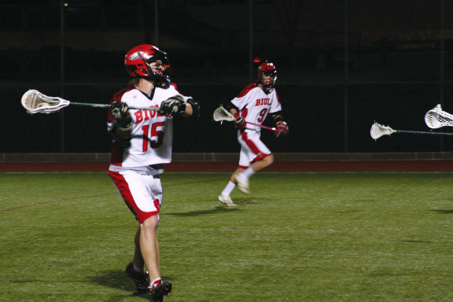 Sophomore midfielder John Crowell (15) cradles the ball in preparing to pass, while freshman midfielder Jon McMahan (9) looks on.