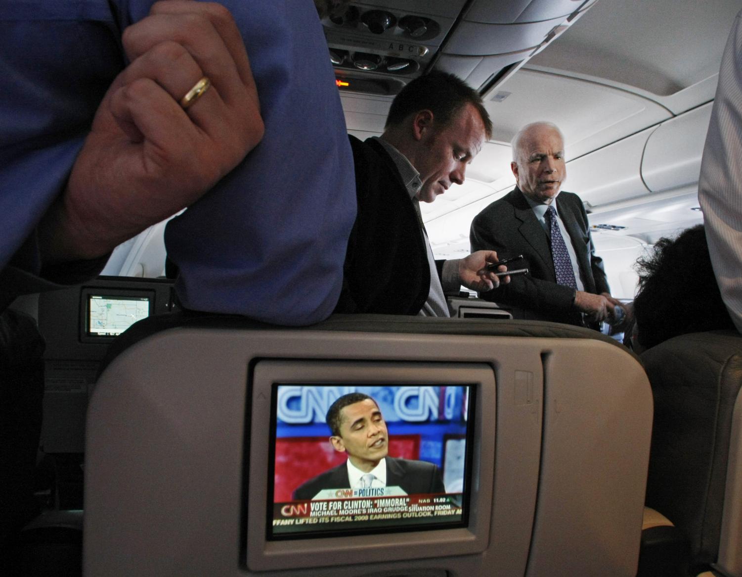 Republican presidential hopeful, Sen. John McCain, R-Ariz., talks with reporters on his campaign plane enroute from Kansas to Seattle, while one of his Democratic rivals, Sen. Barack Obama, D- Ill., is seen on an in flight TV screen Friday, Feb. 8, 2008.