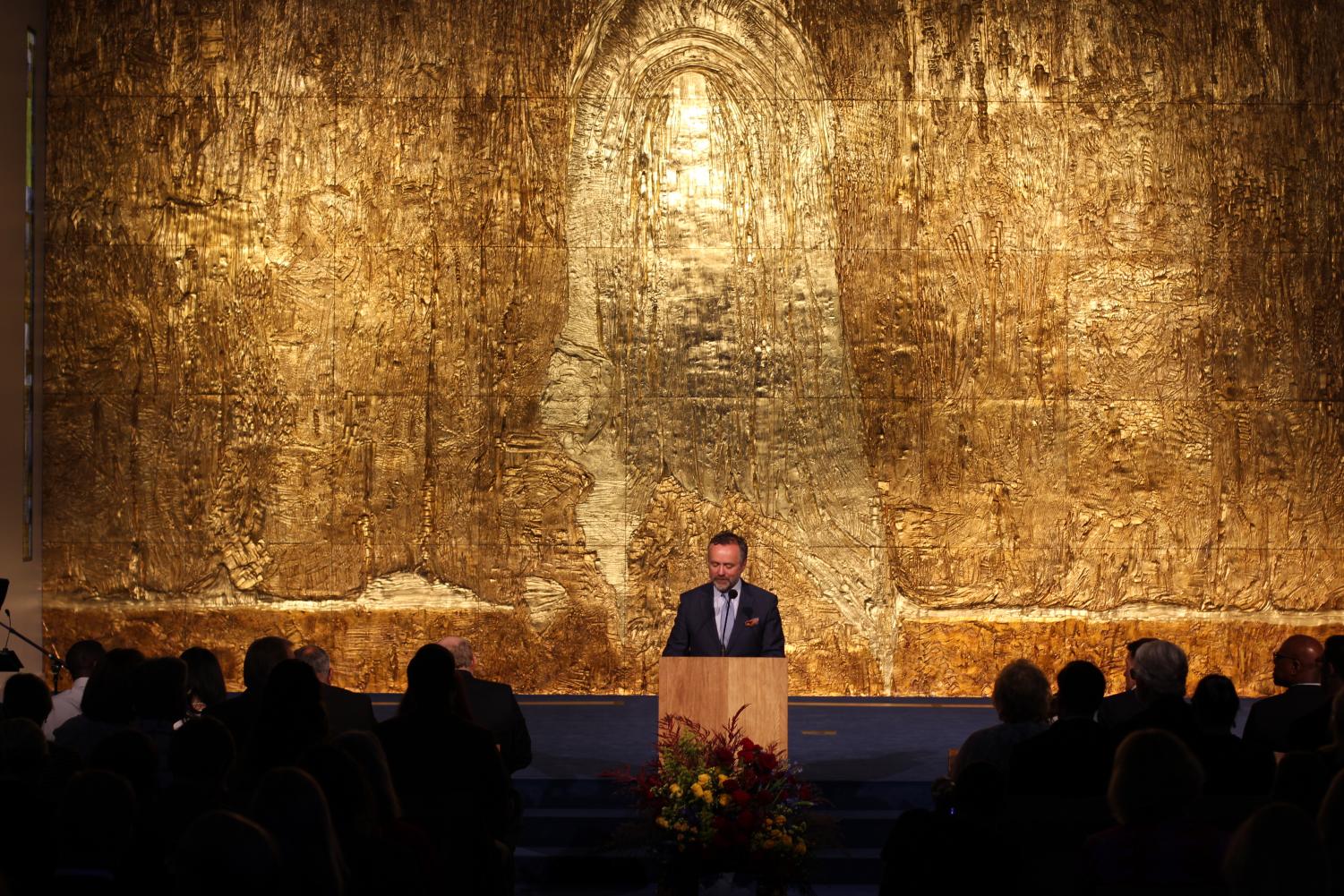 President Barry Corey stands before a 31-foot gold-adorned wall during the dedication ceremony for Calvary Chapel