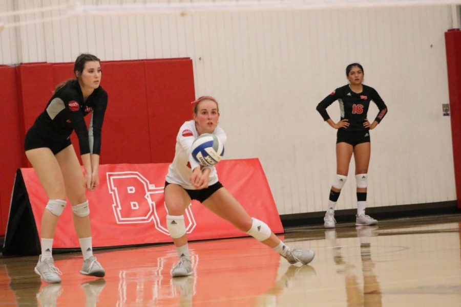Sophomore libero Sami Hover digs a ball out as two other volleyball players watch.