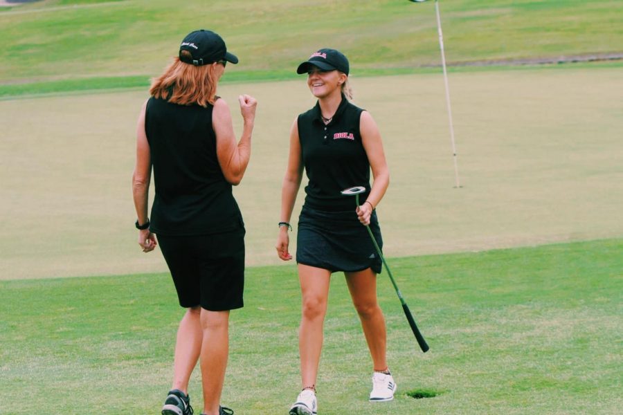 Sophia Karnazes grins on the golf green as coach Jane Carr pumps her fist into the air.